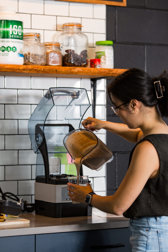 A woman preparing a smoothie in a kitchen.