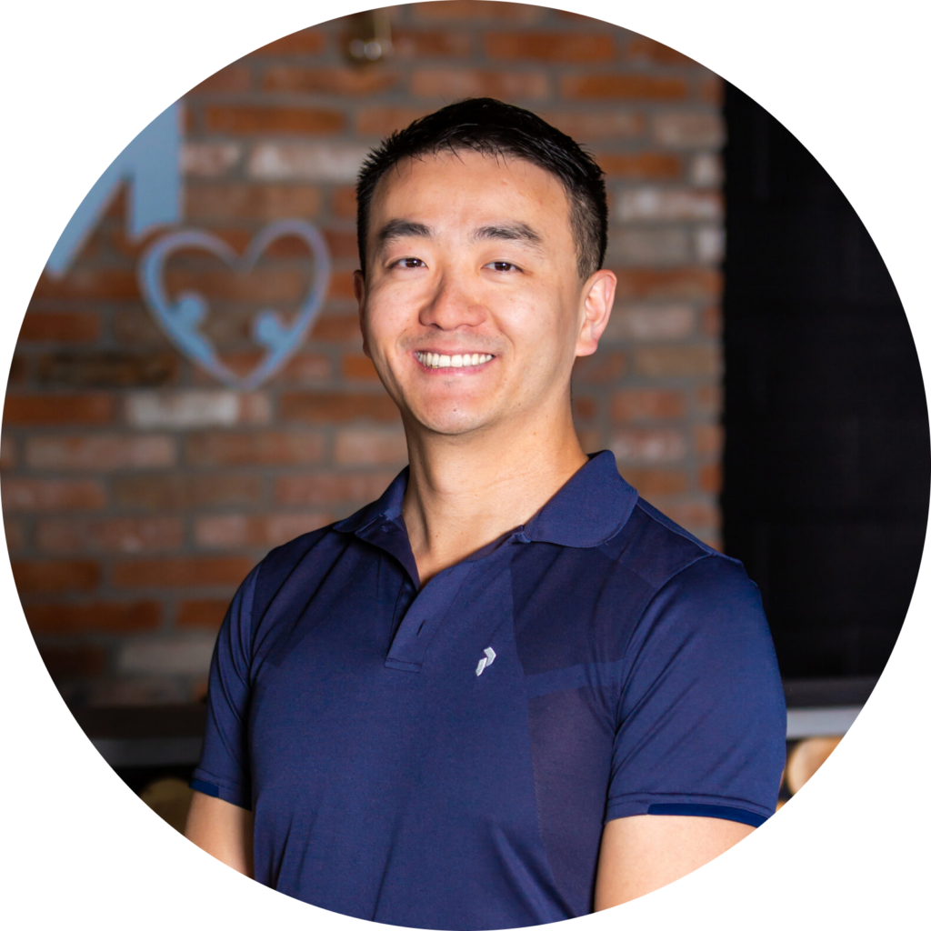 A man in a blue shirt smiling in front of a brick wall.